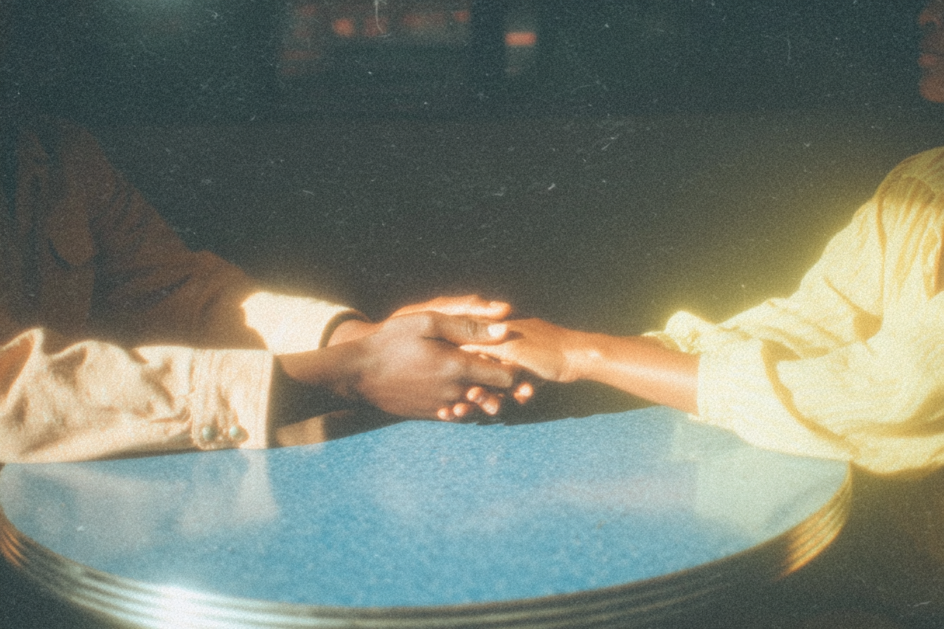 Two hands clasped across a table in warm light.